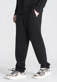 Zwarte kabelgebreide joggers met een ontspannen pasvorm en geribbelde boorden, gecombineerd met gewatteerde witte sneakers met veters.