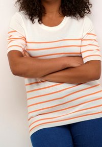 White short-sleeve sweater with orange horizontal stripes, round neckline, ribbed cuffs, and a loose fit, paired with denim blue pants.