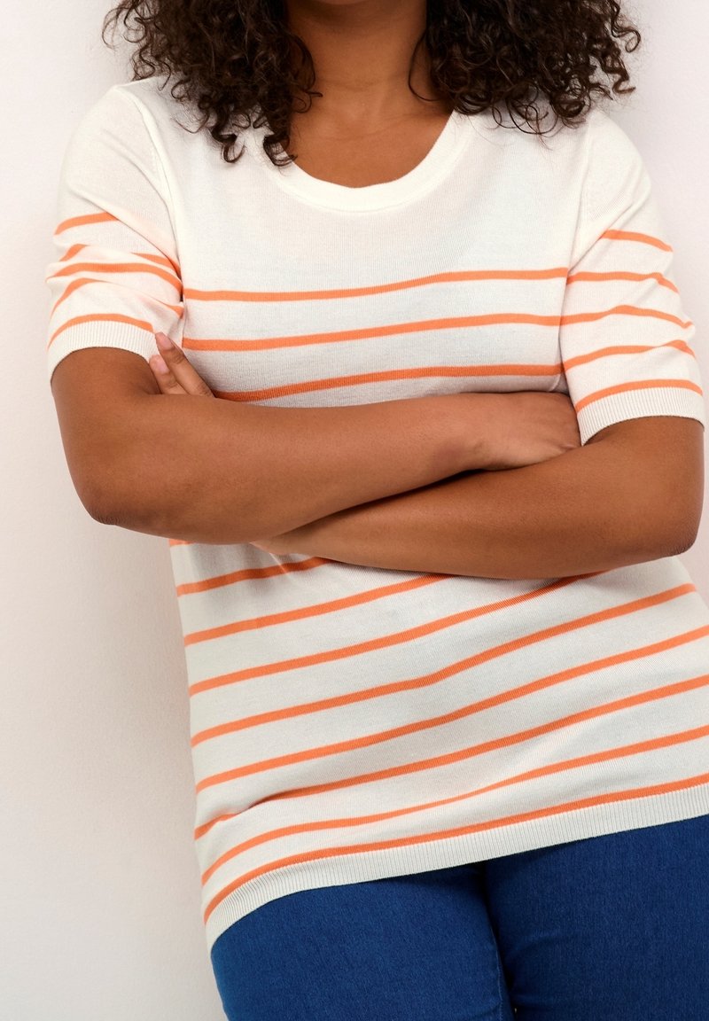White short-sleeve sweater with orange horizontal stripes, round neckline, ribbed cuffs, and a loose fit, paired with denim blue pants.
