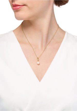 Goldkette mit einem einzelnen weißen Perlenanhänger, getragen von einem Modell in einem weißen V-Ausschnitt-Oberteil. Die Kette ist fein und zart.