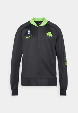 Veste de sport noire avec un col vert, arborant un logo de trèfle, un emblème NBA et l'inscription "BOSTON" sur la manche. Fabriquée en tissu lisse.