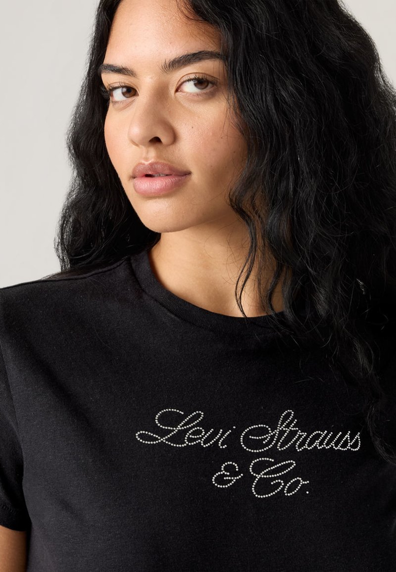 T-shirt noir à manches courtes arborant "Levi Strauss & Co." en strass argentés sur la poitrine. Matière en coton doux avec une coupe classique.