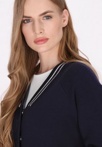 Navyblaue Strickjacke mit V-Ausschnitt und schwarz-weißen gestreiften Rippbündchen. Verfügt über schwarze Knöpfe und ein strukturiertes Strickgewebe.