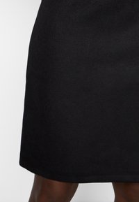 Svart kjol i mjukt tyg med en rak skärning som går ner till mitten av låret. Slät yta utan synliga mönster eller detaljer.