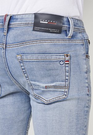 Jeans di denim azzurro chiaro con una texture sbiadita, dotati di una piccola toppa con logo, cuciture a contrasto e due tasche posteriori.
