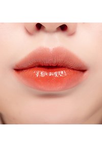 Primer plano de labios gruesos cubiertos con un producto labial naranja brillante, que presenta una textura suave y un degradado de tonos más oscuros a más claros.