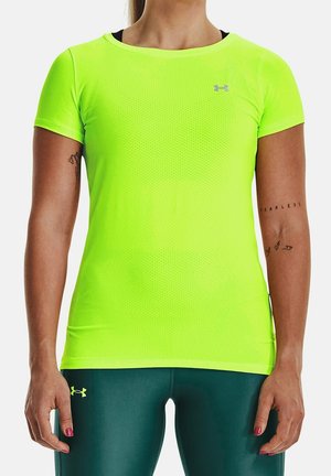 Kvinde iført en klar gul sports t-shirt med korte ærmer og mørkegrønne leggings med synlige tatoveringer på begge underarme.