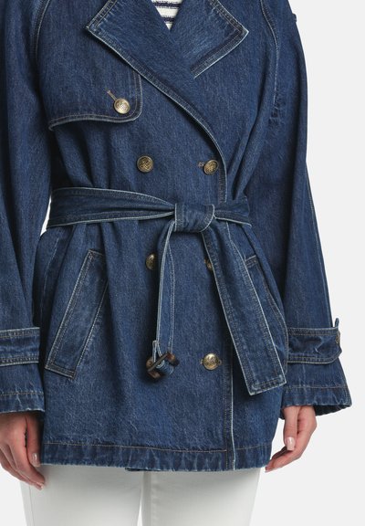 Džínsová bunda tmavomodrej farby s dvojradovým zapínaním na gombíky, pásom v páse, veľkými vreckami a širokými manžetami. Má kontrastné prešívanie a zlaté kovanie.