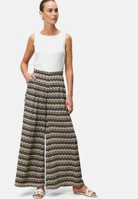 Pantalons larges avec un motif en zigzag beige, marron et blanc. Un haut sans manches blanc uni. Mannequin portant des sandales.