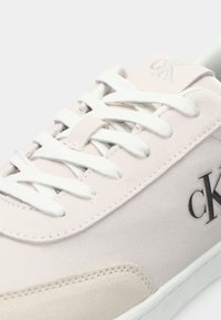 Tenis rosa deschis din suede, cu sireturi și talpă albă, având logo-ul negru "ck" pe lateral și pe limbă.