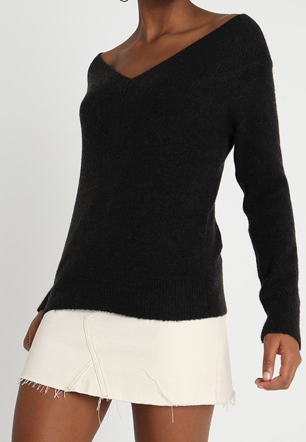 Musta, pehmeä neulepaita, jossa on leveä V-pääntie ja pitkät hihat, yhdistetty valkoiseen minihameeseen, jossa on hapsureuna ja näkyvät saumat.