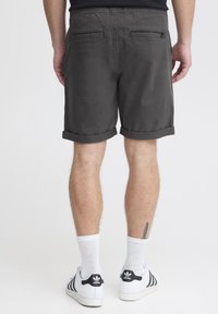 Graue Shorts mit umgeschlagenen Säumen, Gesäßtaschen und elastischem Bund. Getragen mit weißen Sportschuhen und Knöchelsocken.