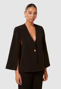 Schwarzer Cape-Blazer mit tiefem V-Ausschnitt, goldenen Knopfverschluss und offenen Seiten. Aus glattem Stoff gefertigt, zeichnet sich durch ein elegantes, modernes Design aus.