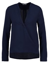 Maglietta lunga blu navy con scollatura a V, design avvolgente e pannello inferiore testurizzato. Tessuto liscio con una leggera lucentezza.