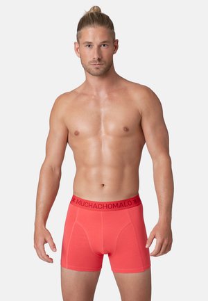 Rote Baumwollboxershorts mit einem elastischen, gebrandeten Bund, die eine enge Passform und eine glatte Textur aufweisen, präsentiert an einem Modell vor einem neutralen Hintergrund.