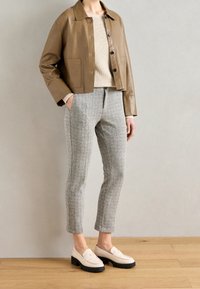 Tan leren jas, beige geribbelde trui, grijs gestreepte broek en crème instappers met zwarte zolen. Eenvoudig, op maat gemaakt ontwerp met knoopdetails.