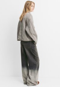 Giacca imbottita grigia oversize con maniche larghe abbinata a jeans a gamba larga neri con sfumature, caratterizzati da un leggero motivo sbiadito e tasche posteriori.