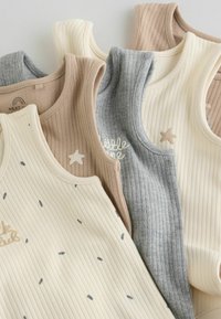 Pile de body bébé sans manches côtelés en beige, crème et gris avec de petits détails d'étoiles et de texte sur une surface blanche.