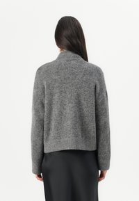 Maglione grigio a maglia con colletto alto, forma svasata e polsini a costine, abbinato a una sottogonna in tessuto nero liscio.