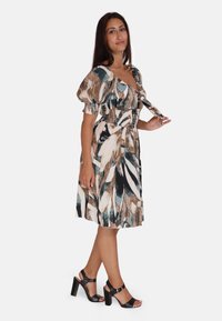 Vestido de longitud hasta la rodilla con estampado floral, mangas abullonadas, bodice smockeado y colores que incluyen verde azulado, marrón y crema, combinado con tacones negros.