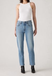 Světle modré džíny z denimu s vysokým pasem, rovnou nohavicí, designem s pěti kapsami a viditelnými švy. V kombinaci s bílým tílkem.