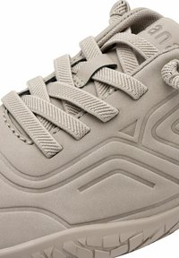 Chaussure de sport beige avec une tige synthétique texturée, des lacets plats et des accents moulés ; présente une semelle courbée avec des motifs de grip.