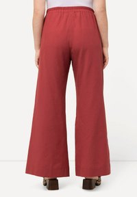 Pantalon large rouge avec une taille élastique, fabriqué dans un matériau léger. Texture lisse et design longueur totale qui s'étend jusqu'aux chevilles.