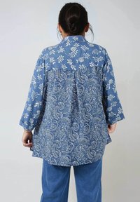Denim shirt with a floral and paisley print, featuring a collar, long sleeves, and a relaxed fit, in shades of blue and white.