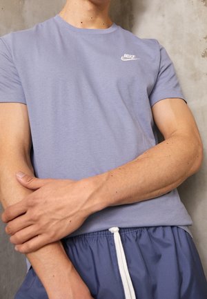 Vaaleansininen Nike T-paita, jossa on pyöreä kaula-aukko ja lyhyet hihat. Rinnassa valkoinen logo. Yhdistetty tummansinisiin shortseihin.