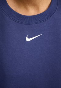Sudadera azul marino con cuello redondo, cuello acanalado y un pequeño logotipo de Nike en blanco en el pecho. Textura de tela suave.