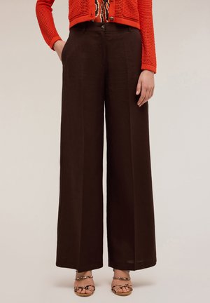 Pantaloni a gamba larga marrone scuro, con chiusura frontale a bottoni e tasche laterali. Abbinati a un cardigan rosso in maglia e a una maglietta con fantasia.