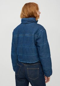 Zniszczona kurtka dżinsowa w ciemnoniebieskim kolorze z pikowanymi panelami, wysokim kołnierzem i elastycznym dołem. Charakteryzuje się gładką fakturą i minimalnymi detalami szycia.