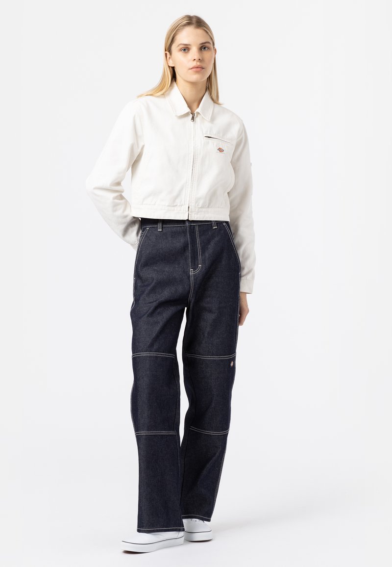 Kortere witte denim jacket met een rits, gecombineerd met high-waisted donkerblauwe jeans met contrasterende stiksels en een losse pasvorm. Witte sneakers.
