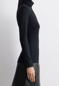 Maglia nera con collo alto in tessuto a coste, caratterizzata da maniche lunghe e un design aderente, abbinata a una gonna di pelle nera.