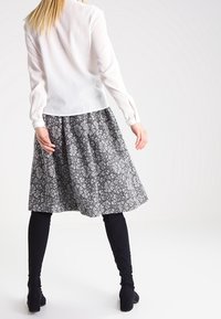 Blouse blanche à manches longues associée à une jupe noire et blanche à motifs, arrivant au genou. La tenue comprend des collants opaques noirs et des bottines.