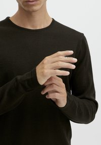 Must proovikangast must pikkade varrukatega särk ümmarguse kaelusega, millel on liibuvad mansetid. Käed on paigutatud nii, et oleks näha nahatooni ja peent tatoveeringut.
