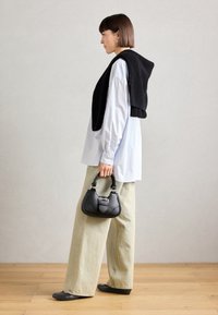 Borsa a tracolla nera in pelle con accessori in argento, abbinata a una camicia bianca oversize e a un maglione nero in maglia appoggiato sulle spalle. Pantaloni chiari.