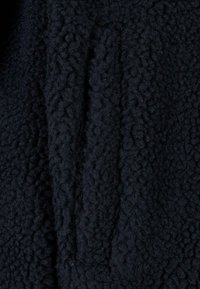 Black fleece fabric featuring a textured surface with a soft, fluffy appearance. The material appears thick and warm, suitable for outerwear.