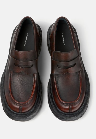 Mocassini in pelle marrone scuro con suole nere spesse e testurizzate, punte arrotondate e dettaglio a fascia sulla parte anteriore, visti dall'alto.