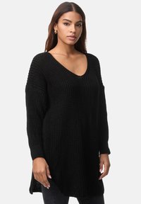 Schwarzer Strickpullover mit V-Ausschnitt, langen Ärmeln und seitlichen Schlitzen. Aus strukturiertem Stoff, mit lockerer, tunikaartiger Passform.