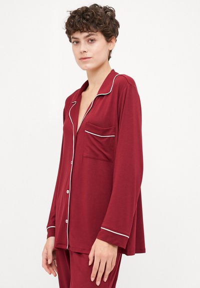 Maroon pajama top with a relaxed fit, white piping along the collar and pocket, long sleeves, and a single chest pocket. Soft material.