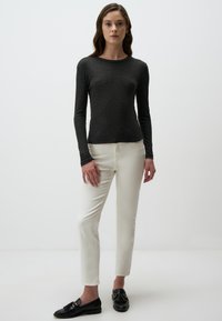 Dunkelgraues Longsleeve-Shirt, taillierte Passform, weicher Stoff. Kombiniert mit weißen Slim-Fit-Hosen und schwarzen Slippern mit dekorativen Akzenten.