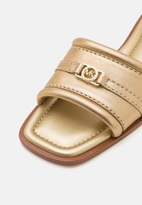 Sandale mule en cuir doré avec un bout carré, dotée de deux brides et d'un accent logo circulaire. Couture subtile le long des bords.