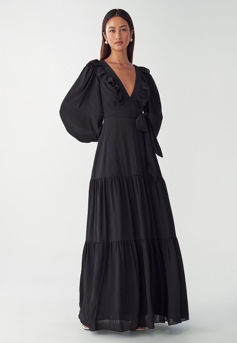 Black maxi dress made of lightweight fabric, featuring a deep V-neck, ruffled details on the bodice, and long billowy sleeves with a tiered skirt.