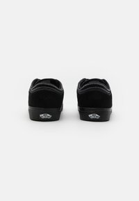 Sorte semskede joggesko med lavt design, flat gummisåle, kontrasterende hvite sømmer og en merket hæltabs med teksten 'Vans Off the Wall.'