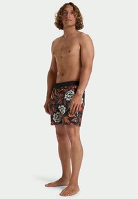 Costumi da bagno floreali neri con motivi arancioni e bianchi. Presentano una vita elasticizzata e sono realizzati in materiale leggero.