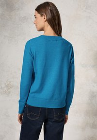Maglione blu a maglia con scollatura e orlo a costine. Il tessuto testurizzato presenta un leggero motivo a macchie. Vista posteriore che mostra il design aderente.