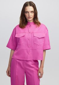 Roze cropped shirt met een mandarin kraag, korte mouwen, twee borstzakken en een knoopsluiting aan de voorkant. Soepele textuur, minimalistisch ontwerp.