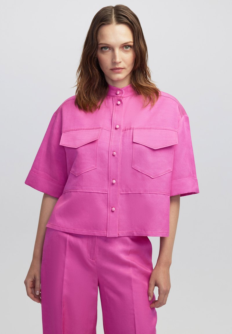 Roze cropped shirt met een mandarin kraag, korte mouwen, twee borstzakken en een knoopsluiting aan de voorkant. Soepele textuur, minimalistisch ontwerp.