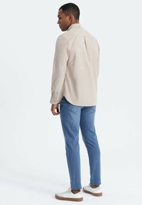 Beige overhemd met lange mouwen, een button-down kraag, een rugplooitje en knopen bij de mouwen, gecombineerd met blauwe jeans en witte sneakers.